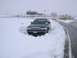 1999 Ford Crown Victoria - A dark 1999 Ford Crown Victoria is partially buried in snow, showing its front grille and headlights.