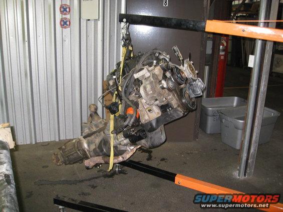 Engine and transmission assembly suspended by a yellow strap and engine hoist