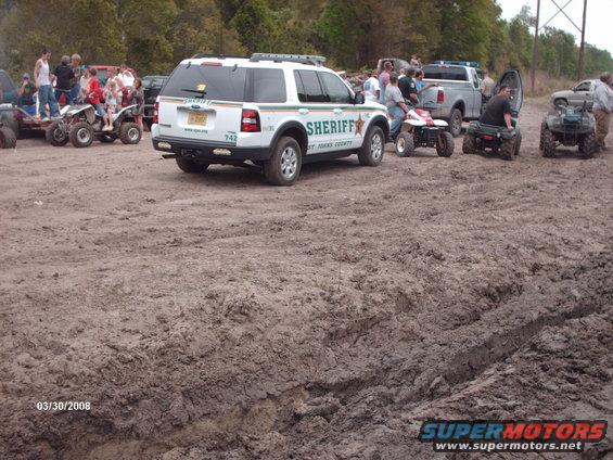 Sheriff's SUV parked in mud with ATVs and people around
