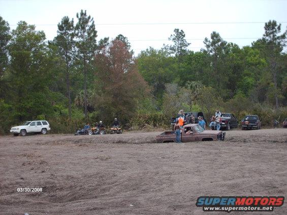Rusty pickup truck stuck in mud with people around it