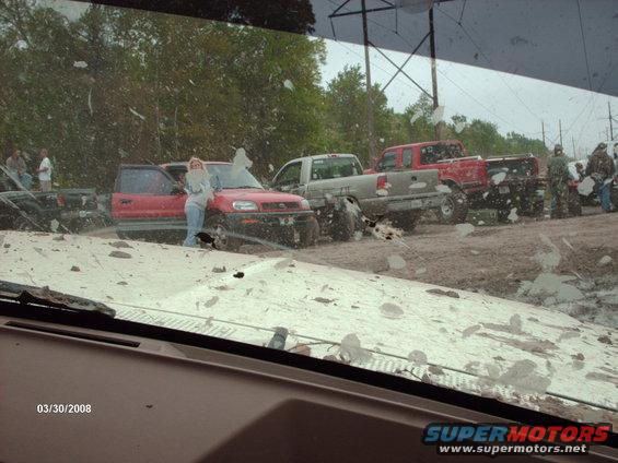 Muddy scene with a red SUV and several trucks, people standing around. Date stamp 03/30/2008