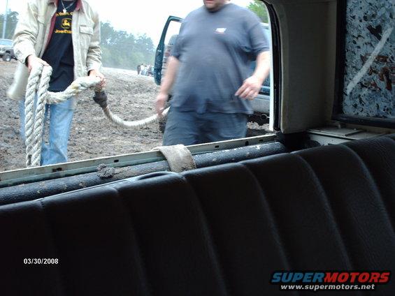 Two guys with a rope in a muddy field, one is wearing a John Deere shirt. Another truck is visible in the background