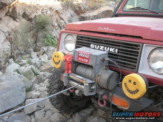 Red Suzuki Samurai on rocky terrain with a winch and smiley face lights