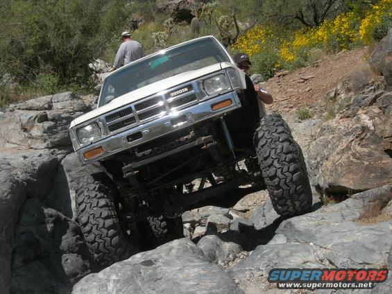 White Toyota pickup with big tires climbing over rocks. Someone is standing on the driver's side