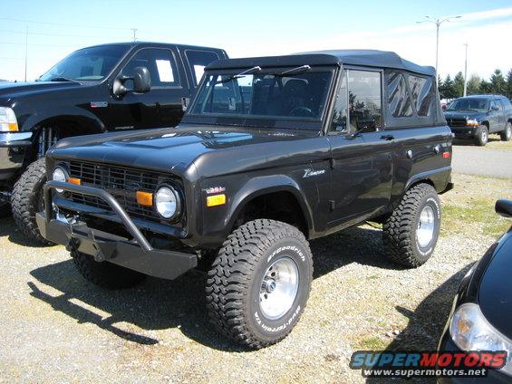 Black Ford Bronco with aftermarket bumper and large tires parked next to a black pickup truck