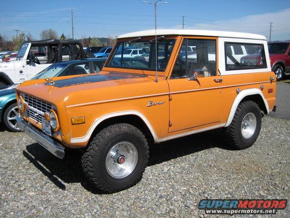 Orange 1978 Ford Bronco with a white hardtop, parked on gravel