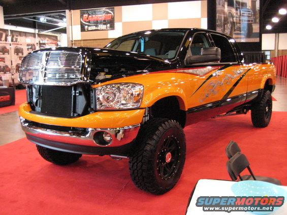 Lifted pickup truck with orange and black custom paint, large chrome grille, and aftermarket wheels