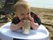 1990 Ford Bronco - A baby sits in a high chair on the sand, curiously examining a beverage can.