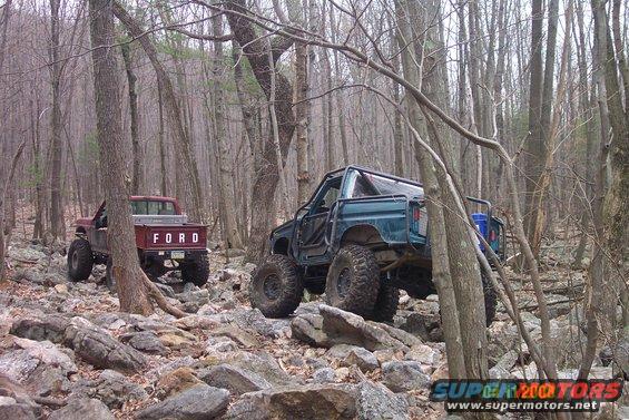 Teal off-road SUV and red Ford pickup truck on a rocky trail in a forest