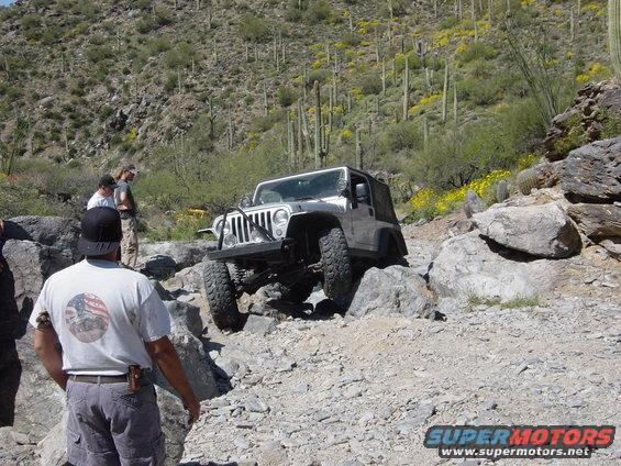 Silver Jeep Wrangler navigating a boulder-strewn desert path with saguaro cacti in the background