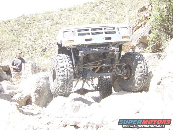 Modified off-road vehicle with large tires climbing over rocks on a desert trail