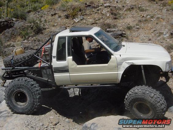 White pickup truck with roll cage and large tires on rocky terrain