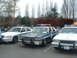 1987 Ford Crown Victoria LTD - Three police cars are parked side-by-side in a lot, with trees and a hedge in the background.