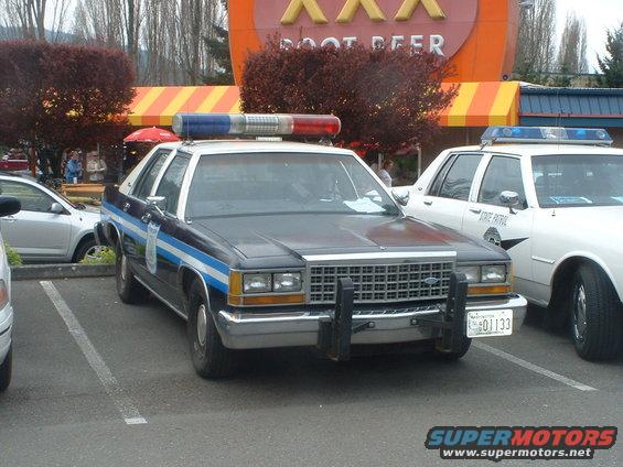 Dark blue and white police car with light bar and push bumper, parked next to a white state patrol car