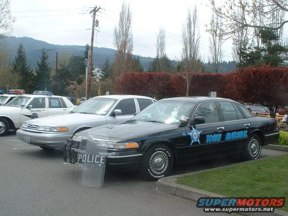 Two police cars parked, one black Town Marshal car with a shield, one silver car with 'POLICE' on shield