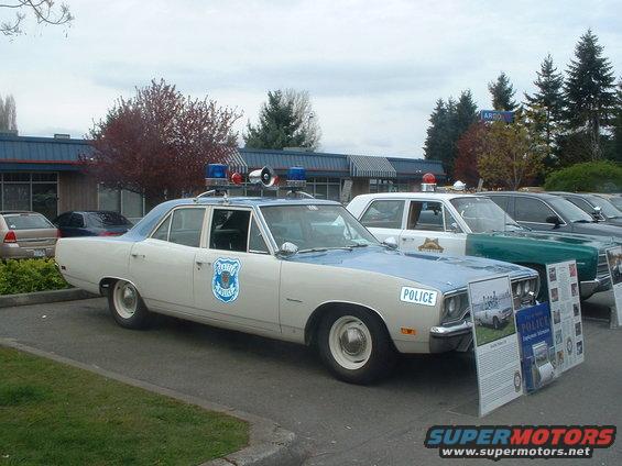 Cream and light blue police car with light bar, parked next to other vehicles