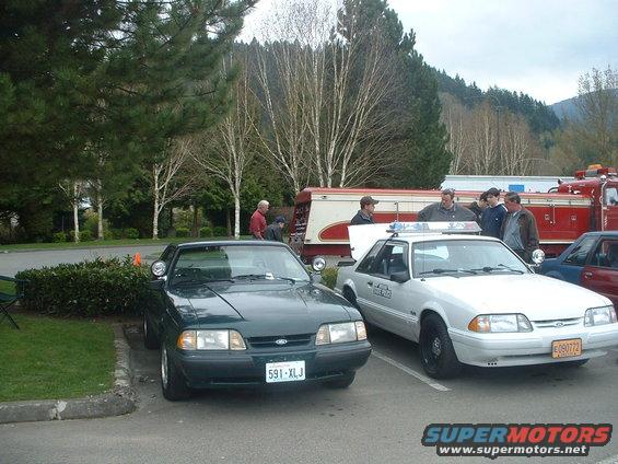 Green 1987 Ford Mustang parked next to a white 1987 Ford Mustang police car and a fire truck