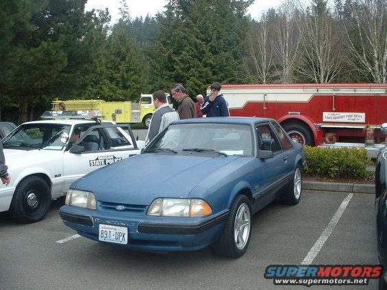 Blue 1987 Ford Mustang parked next to a white Oregon State Police car. A fire truck is in the background