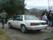 1987 Ford Crown Victoria LTD - A white coupe is parked outdoors with people around it and mountains in the background.