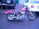 1972 Harley-Davidson Super Glide - A pink motorcycle is parked on a wet asphalt surface, with a white car and a dark SUV in the background.