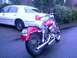 1972 Harley-Davidson Super Glide - A pink motorcycle is parked behind a white sedan on a wet street.