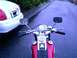 1972 Harley-Davidson Super Glide - Motorcycle handlebars and gauge with a white car parked nearby on a wet road.