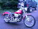 1972 Harley-Davidson Super Glide - A red 1972 Harley-Davidson Super Glide motorcycle is parked on a wet road, with a black SUV in the background.