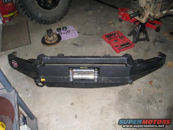 Black custom front bumper with a winch and tow hooks, on a concrete floor