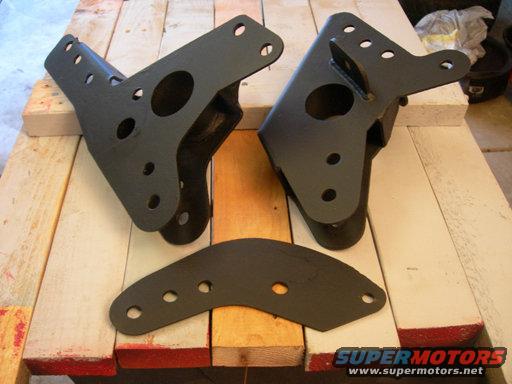 Three black metal suspension brackets on a wooden surface. Two are angled, one is flat