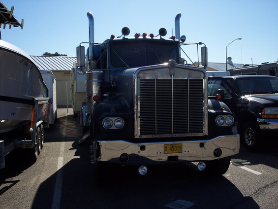 Front view of a dark blue semi-truck with a chrome grille and dual exhaust stacks