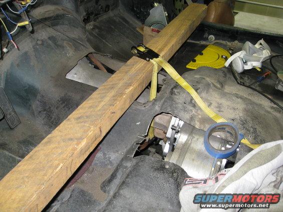 Vehicle interior with wooden beam and straps supporting the floor pan, showing exposed mechanical parts