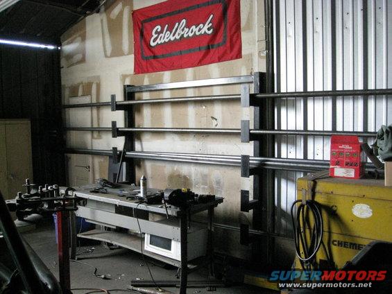Workshop interior with Edelbrock banner, metal storage racks, workbench, and welding equipment