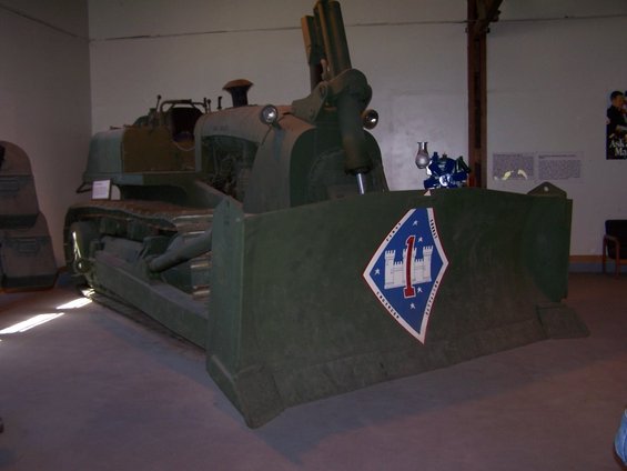 Green bulldozer with a large blade displaying a military emblem