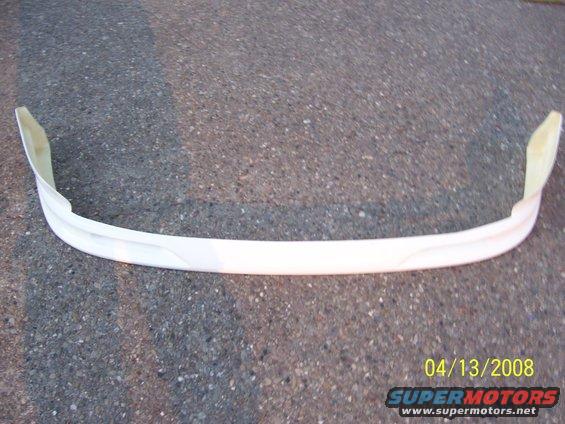 White car bumper part on asphalt. The part is curved and has visible mounting tabs on the ends