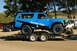 1986 Ford Bronco - A modified blue Bronco is loaded onto a trailer, with other vehicles visible in the background.
