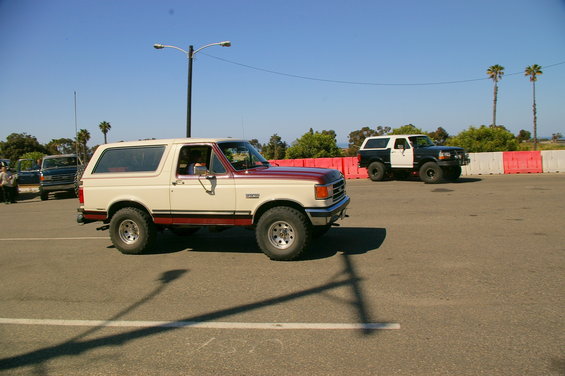 Cream and maroon Ford Bronco driving, another black and white Bronco behind it