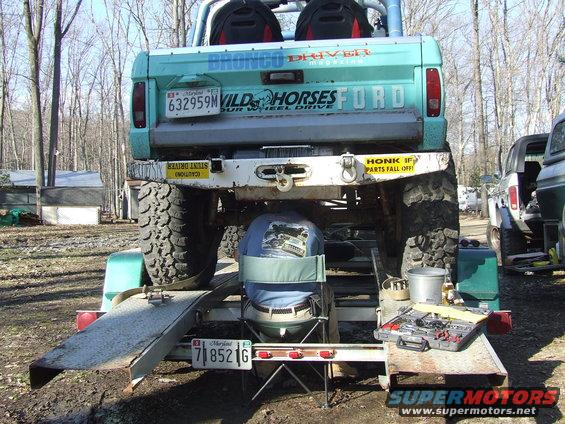 Rear view of a teal Ford Bronco on a trailer, with tools and another vehicle nearby