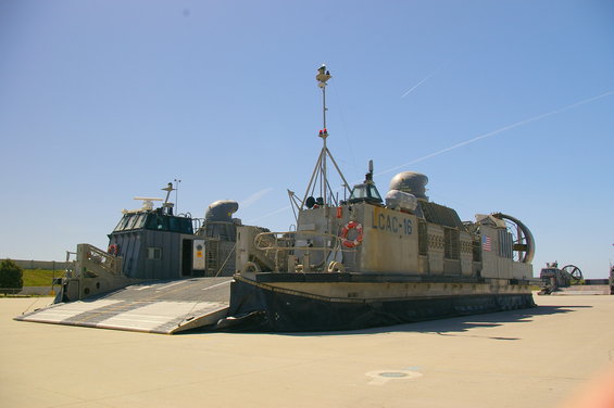 Two landing craft air cushion vehicles parked on pavement under a clear blue sky. One has 'LCAC-16' visible