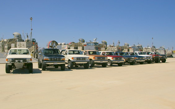White Ford F-150 pickup truck with aftermarket bumper and lights, parked on sand