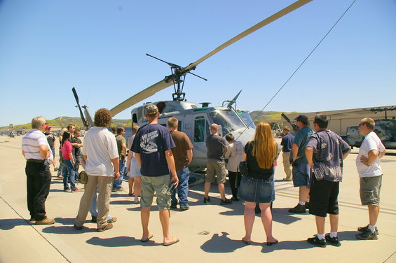 Gray helicopter on tarmac with people gathered around, viewed from the front-right