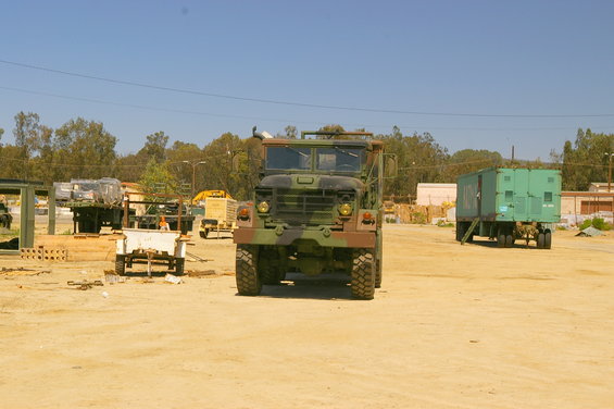 Front view of a camouflage military truck parked in a lot with other vehicles and trailers