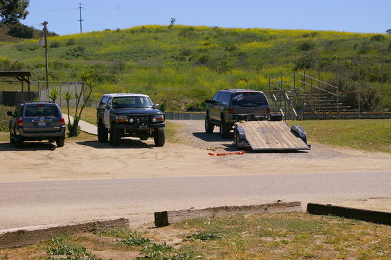 Three SUVs parked in a lot with a trailer attached to one; grassy hill in background
