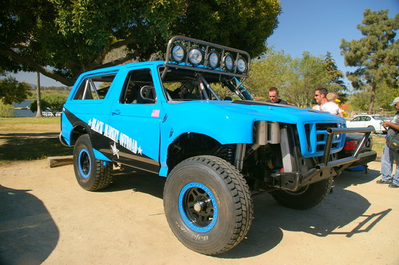 1986 Ford Bronco modified for off-road, painted bright blue with black graphics and "Black Market Offroad" text. Features a roll cage, light bar, and large tires