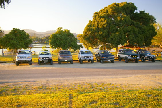 Line of SUVs and trucks parked by a lake at sunset