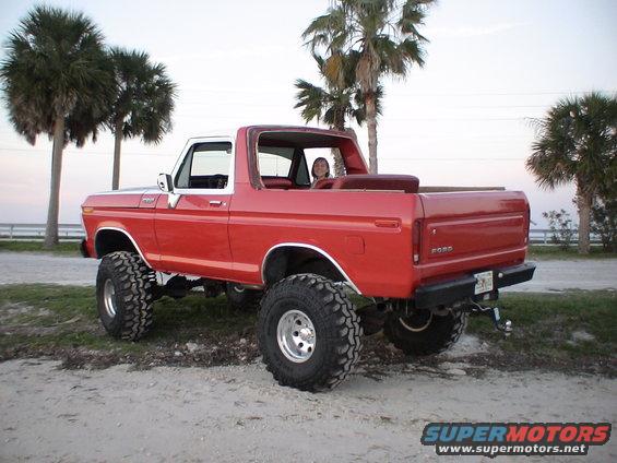Red lifted 1978 Ford Bronco with white top parked on dirt near palm trees