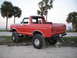 1978 Ford Bronco - A lifted red Ford Bronco with a white top is parked on a sandy area with palm trees in the background.
