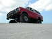 1978 Ford Bronco - A red 1978 Ford Bronco navigates a sandy terrain, with one wheel partially submerged.