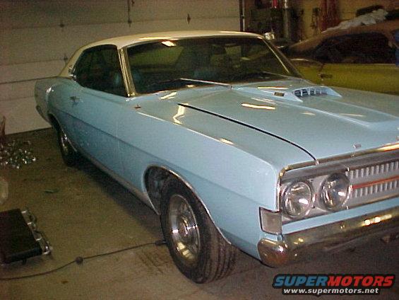 Light blue coupe with white roof, hood scoop, and chrome trim. It has a prominent grille and dual headlights