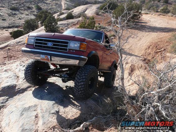 Red 1987 Ford Bronco with oversized tires navigating rocky terrain