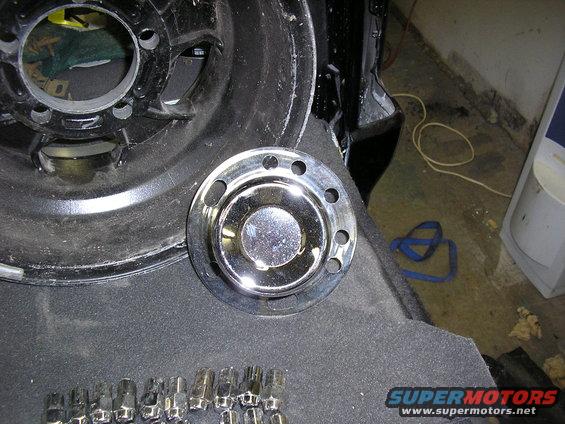 Chrome wheel hubcap and lug nuts on dark carpeted surface